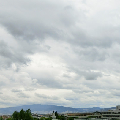 写真の下側に町並みと山、空は雲で覆われています。