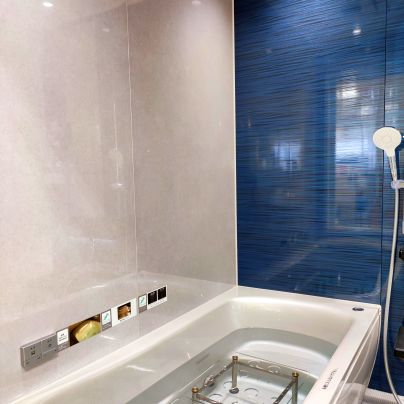 ＴＯＴＯのシステムバス。白い浴槽で、長手側の壁は白いパネルで銀色の操作盤がついています。短手側の壁は紺色のパネルに白いシャワーがついています。