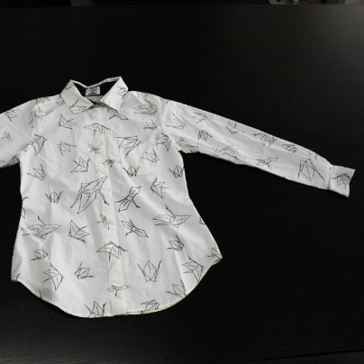 黒い机のうえに白いシャツ、シャツには折り鶴のプリントがたくさんあります。