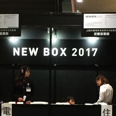 黒字の壁に白い文字でNEW BOX 2017と書いた前で黒い受付机を前に二人の女性が立っています。
