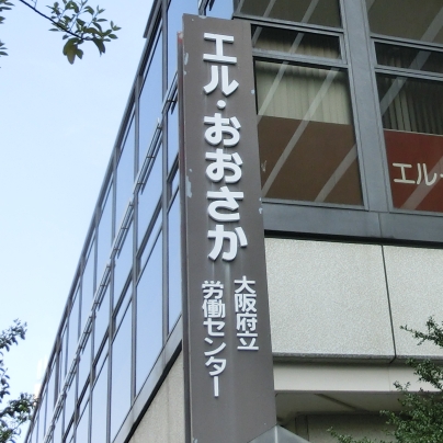 濃い褐色で縦長の看板に白い文字でエル・おおさか 大阪府立労働センターと書いてあります。