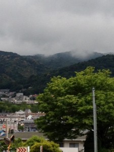緑の木々が鮮やかな山の山頂付近にうっすらと雲がかかっているようすと麓の町並み。
