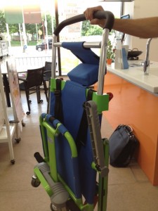 緑色のフレームに青いシートがついた非常時脱出用の車椅子を折りたたんだ様子