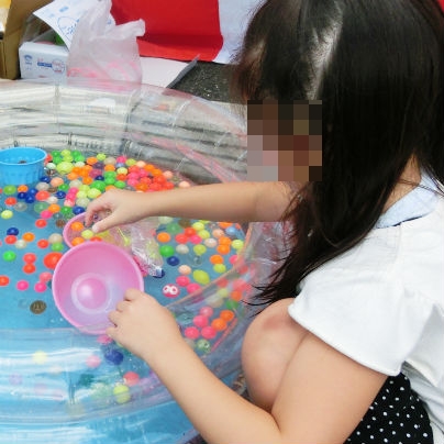 子供用のプールにたくさんのスーパーボールを浮かべ、女の子がピンクのボウルをもって掬っています。