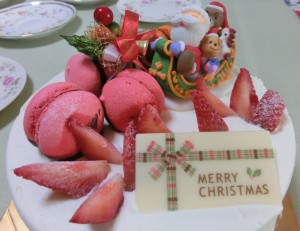 白いケーキの上に、赤いイチゴと赤いマカロン、そしてクリスマスケーキにはMerry Christmasと書いたチョコレートが載っています