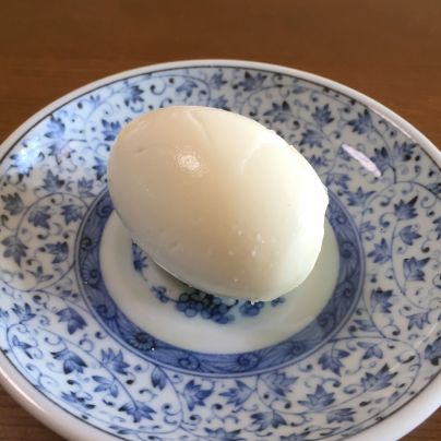 木製の机のうえに青色と白色のお皿が１つ。その上に白いゆで卵のむき身が１つ置いてあります。
